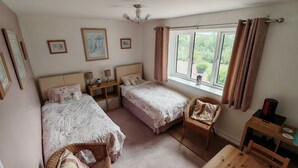 Een slaapkamer met twee bedden, een nachtkastje, een stoel, een tafel en een raam met gordijnen.