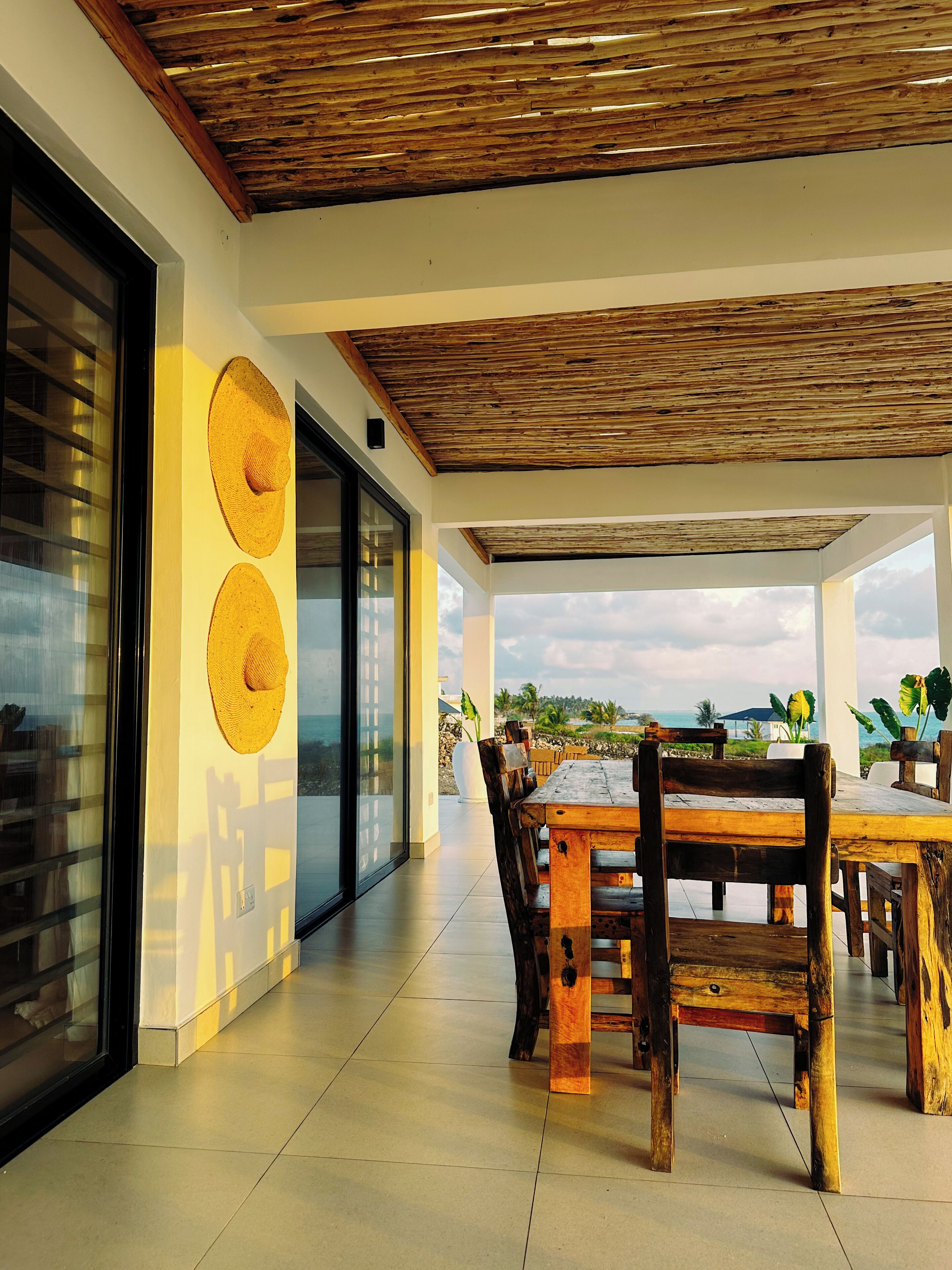 A spacious patio with a wooden table and chairs, a large window, and a view of the ocean.