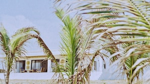 A white building with a flat roof and a balcony with chairs. Palm trees are in the foreground. - Villa Kweli (Makunduchi)