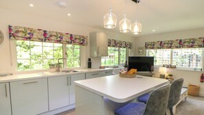 Une cuisine moderne avec des meubles blancs, un grand îlot central, des tabourets de bar et un téléviseur.