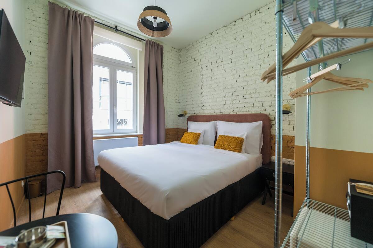 A hotel room with a large bed, a desk with a chair, a TV, and a window with curtains.