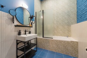 Un baño con un lavabo blanco, repisas negras, un espejo redondo y una ducha con cerramiento de vidrio.