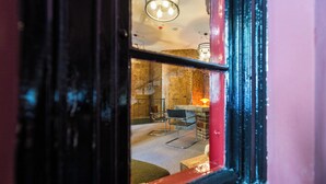A view through a window with a metal frame, revealing a room with a brick wall, a wooden floor, and a chair. - East-West Boutique Hotel Budapest (Budapest)