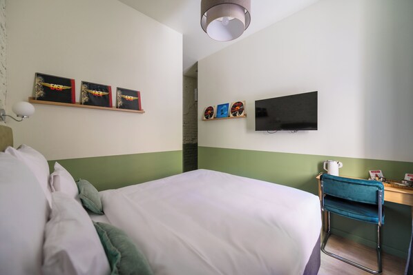A hotel room with a bed, a desk with a chair, a flat-screen TV, and artwork on the walls.
