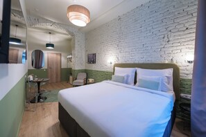 Una habitación de hotel con una cama grande, una mesita pequeña, una silla, un espejo y una pared de ladrillo.