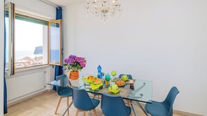 Een moderne eetruimte met een glazen tafel, blauwe stoelen en een kroonluchter.