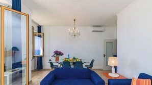 Een moderne woonkamer met een glazen eettafel, blauwe banken en een kroonluchter.