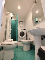 A bathroom with a toilet, bidet, washing machine, and a mirror.