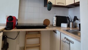 Cozinha compacta com micro-ondas, pia pequena, um banquinho de madeira e escorredor de louça.