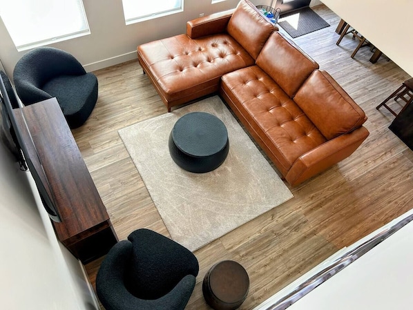 A modern living room with a sectional sofa, two armchairs, a coffee table, and a wooden floor.