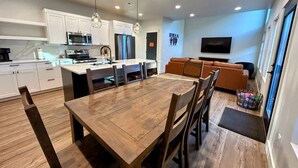 A modern kitchen with white cabinets, a wooden dining table, and a built-in oven.
