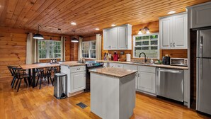 A wooden-paneled kitchen with white cabinets, stainless steel appliances, and a central island. - 15 MINUTES FROM ASHEVILLE! Secluded peacefull LOG CABIN (Leicester)