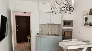 Een compacte keuken met een magnetron, oven en een spoelbak. Er is een eettafel met stoelen en een kroonluchter erboven.