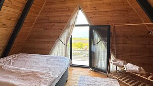 Une chambre confortable située sous les toits, avec un grand lit, un plancher en bois et une vue dégagée grâce à une porte ouverte.