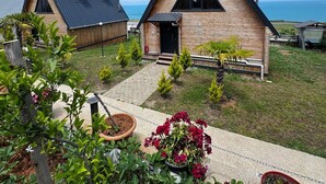 Une maison moderne avec un toit triangulaire, un porche à l’avant et un petit jardin agrémenté de plantes en pot.