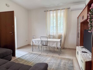 Un'area pranzo con tavolo e sedie, un divano, un mobile contenitore e una TV.