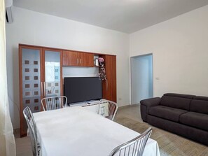 Un soggiorno con divano, un tavolo da pranzo con sedie e una televisione.