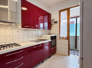 Una cucina con mobili rossi, piano cottura a gas, forno e una finestra con tenda.