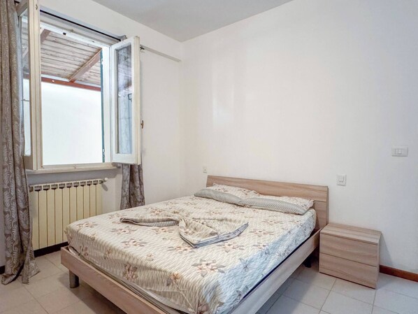 Un dormitorio con cama de madera, una ventana con cortinas, un radiador y una mesita de noche de madera.