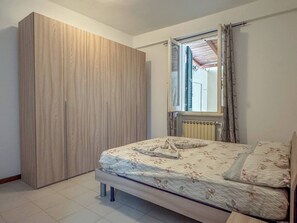 Makuuhuone, jossa on sänky, vaatekaappi, ikkuna verhoilla ja patteri.