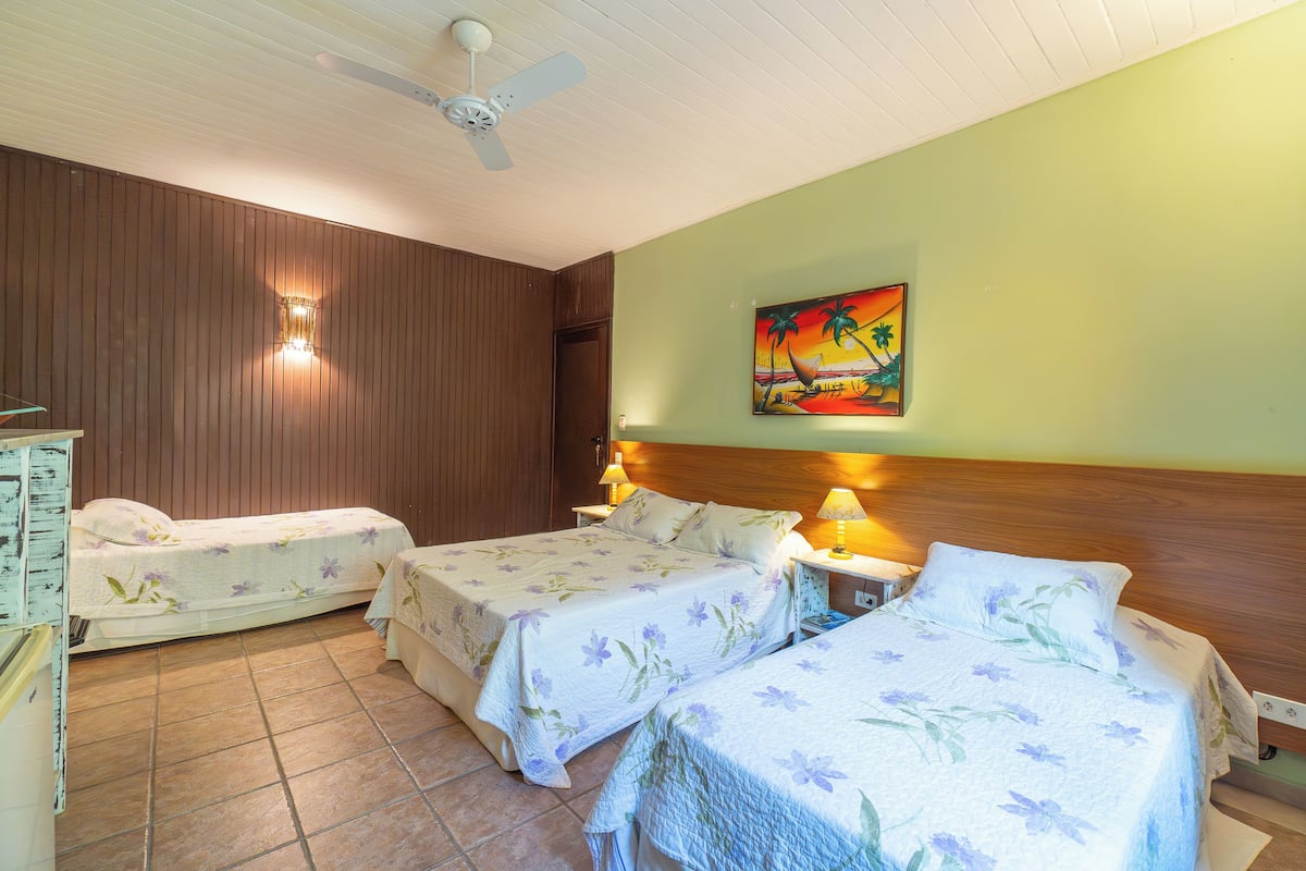 Habitación de hotel con dos camas, paneles de madera en las paredes, ventilador de techo y un cuadro colgado.