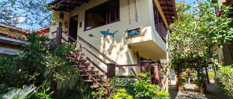 Una casa de dos pisos con techo de tejas, una escalera que conduce al nivel superior y un balcón con esculturas decorativas de peces.