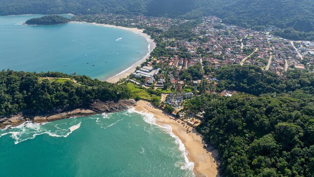 An aerial view of a coastal town with a beach, dense greenery, and a mountainous backdrop. - Vivenda do Flamboyant  (Ubatuba)