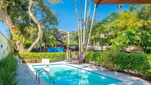 A rectangular swimming pool with a clear blue water, surrounded by lush greenery and trees. - Vivenda do Flamboyant  (Ubatuba)
