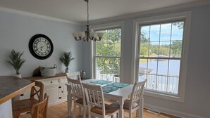 A dining area with a wooden table, white chairs, and a view of a lake through large windows.