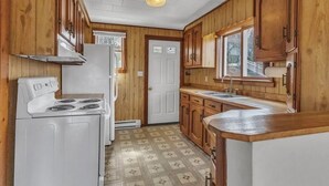 Una cocina compacta con armarios de madera, una estufa blanca y un lavamanos.