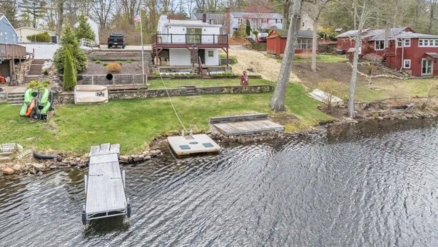 Propiedad frente al lago con muelle, un bote pequeño y una zona verde con terraza de madera.