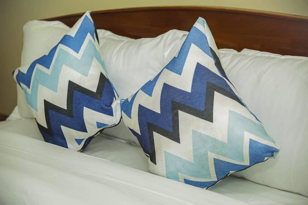 Un lit avec une literie blanche et deux oreillers à motifs en zigzag.