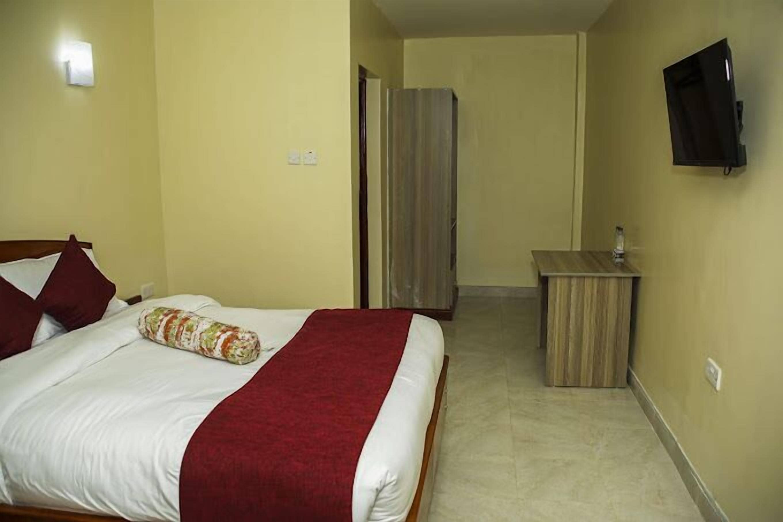 A hotel room with a bed, a small desk, and a TV mounted on the wall.