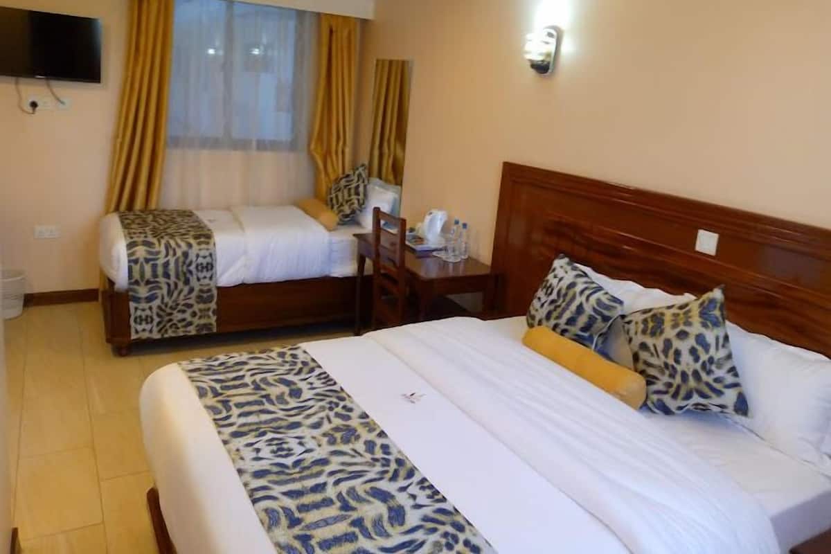 Une chambre d’hôtel avec deux lits, un téléviseur fixé au mur et une fenêtre avec des rideaux.