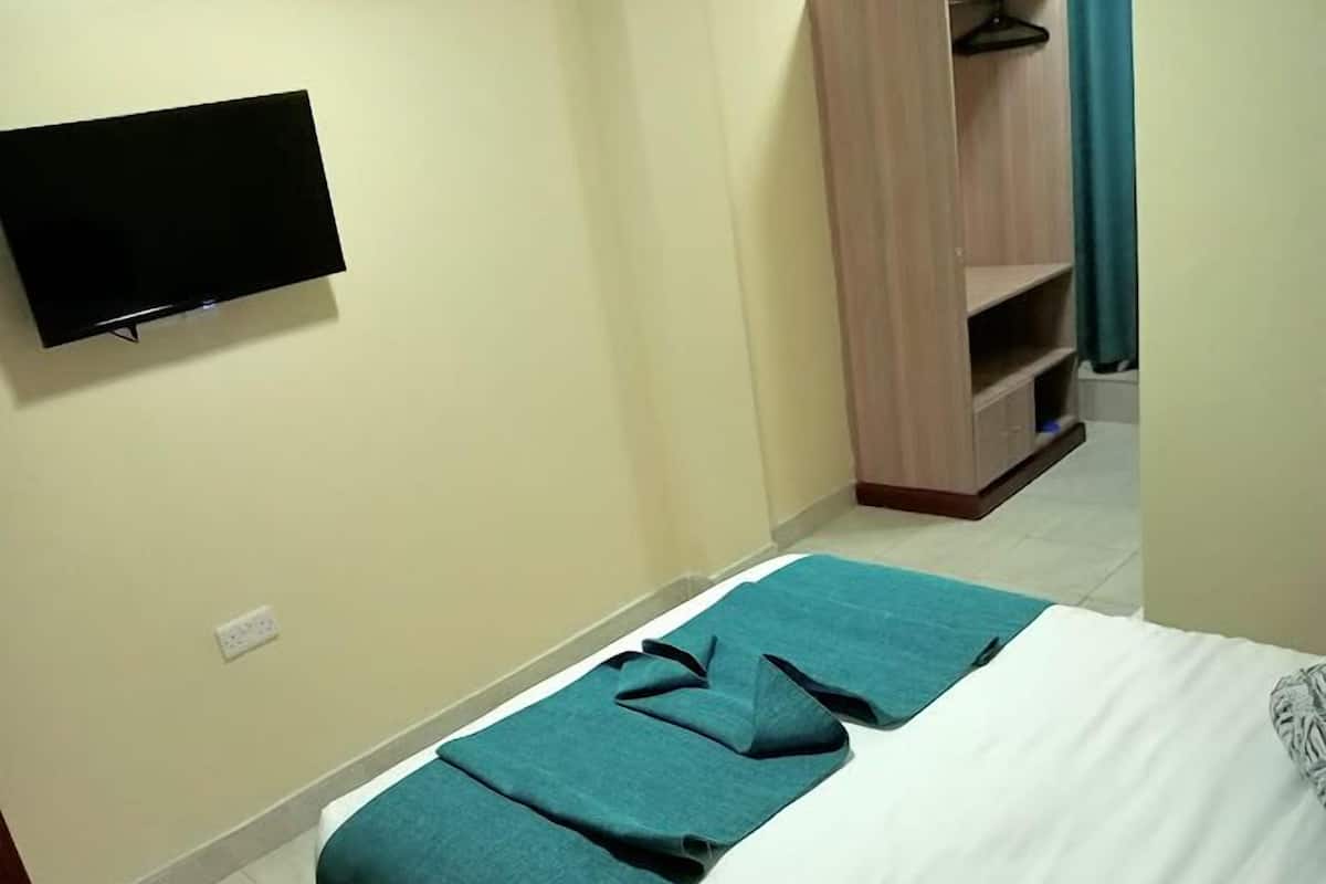 Une chambre d’hôtel avec un lit, un téléviseur fixé au mur et une armoire.