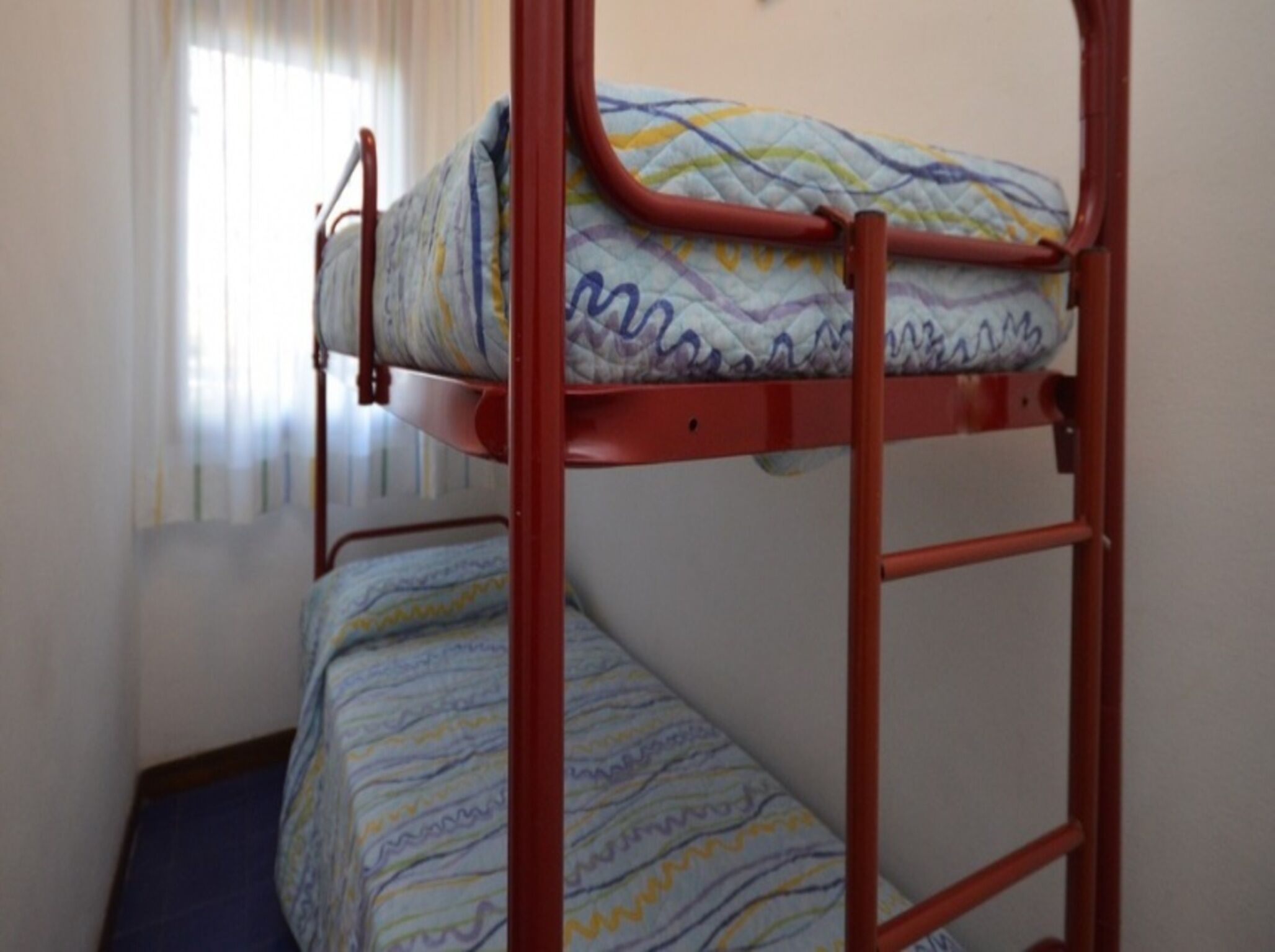 Un lit superposé avec un matelas à motifs dans une pièce dotée d’une fenêtre et de rideaux.