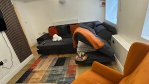 Una sala de estar moderna con un sofá modular, una mesita con aperitivos, una alfombra colorida y un amplio ventanal con persianas.