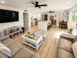 Ein modernes Wohnzimmer mit Fernseher, Sofa, Couchtisch und einer Küche im Hintergrund.