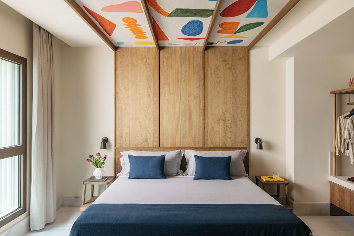 Un dormitorio moderno con una cama grande, cabecera de madera y un diseño de techo colorido.