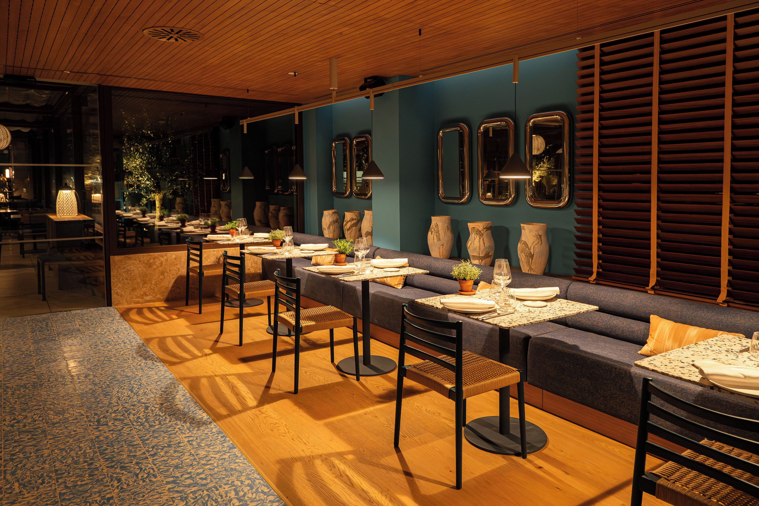 Un restaurante con varias mesas y sillas, una pared azul decorativa y jarrones ornamentales.