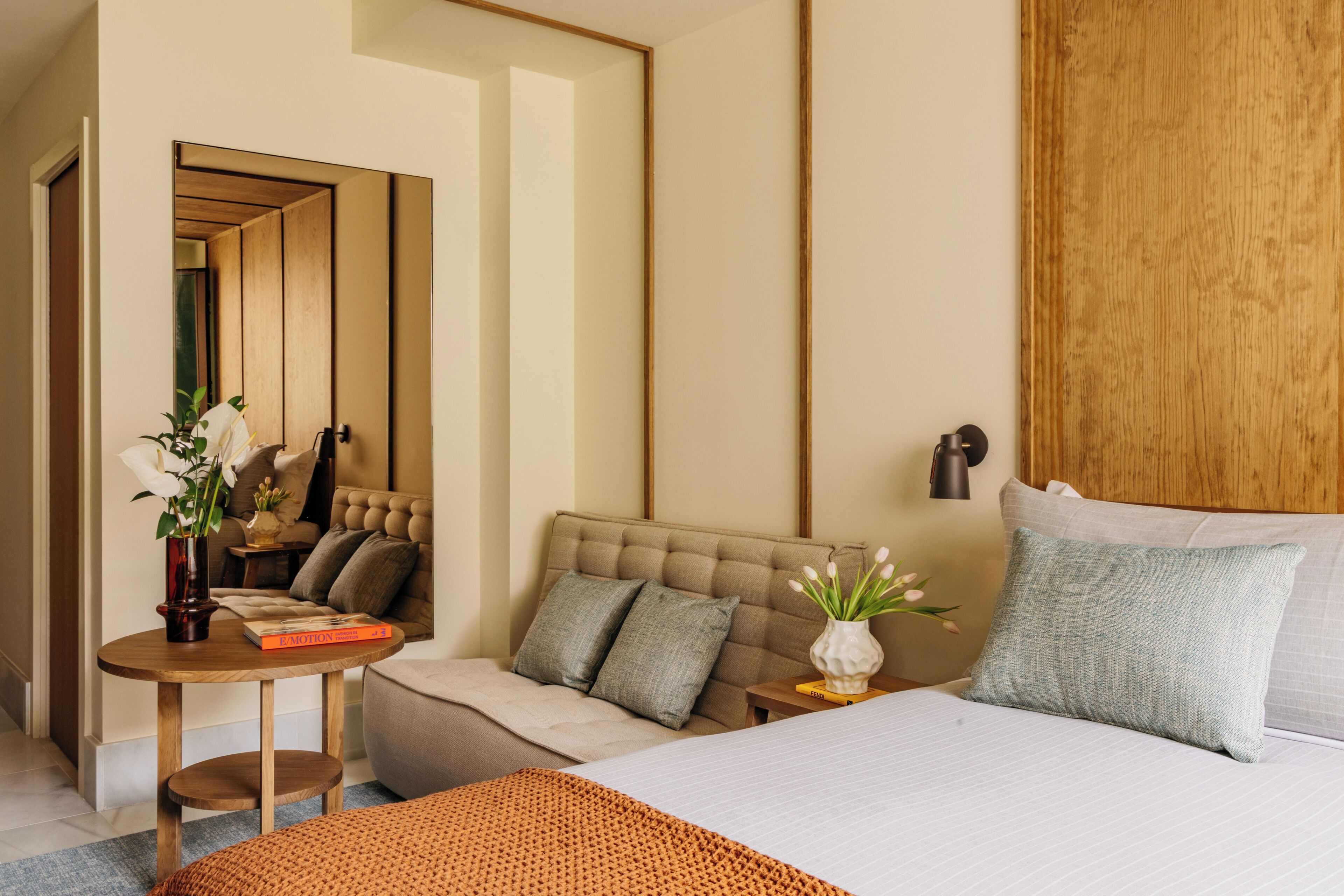 Ein Hotelzimmer mit einem Bett, einem Sofa, einem kleinen Tisch mit einer Vase und einem Spiegel.