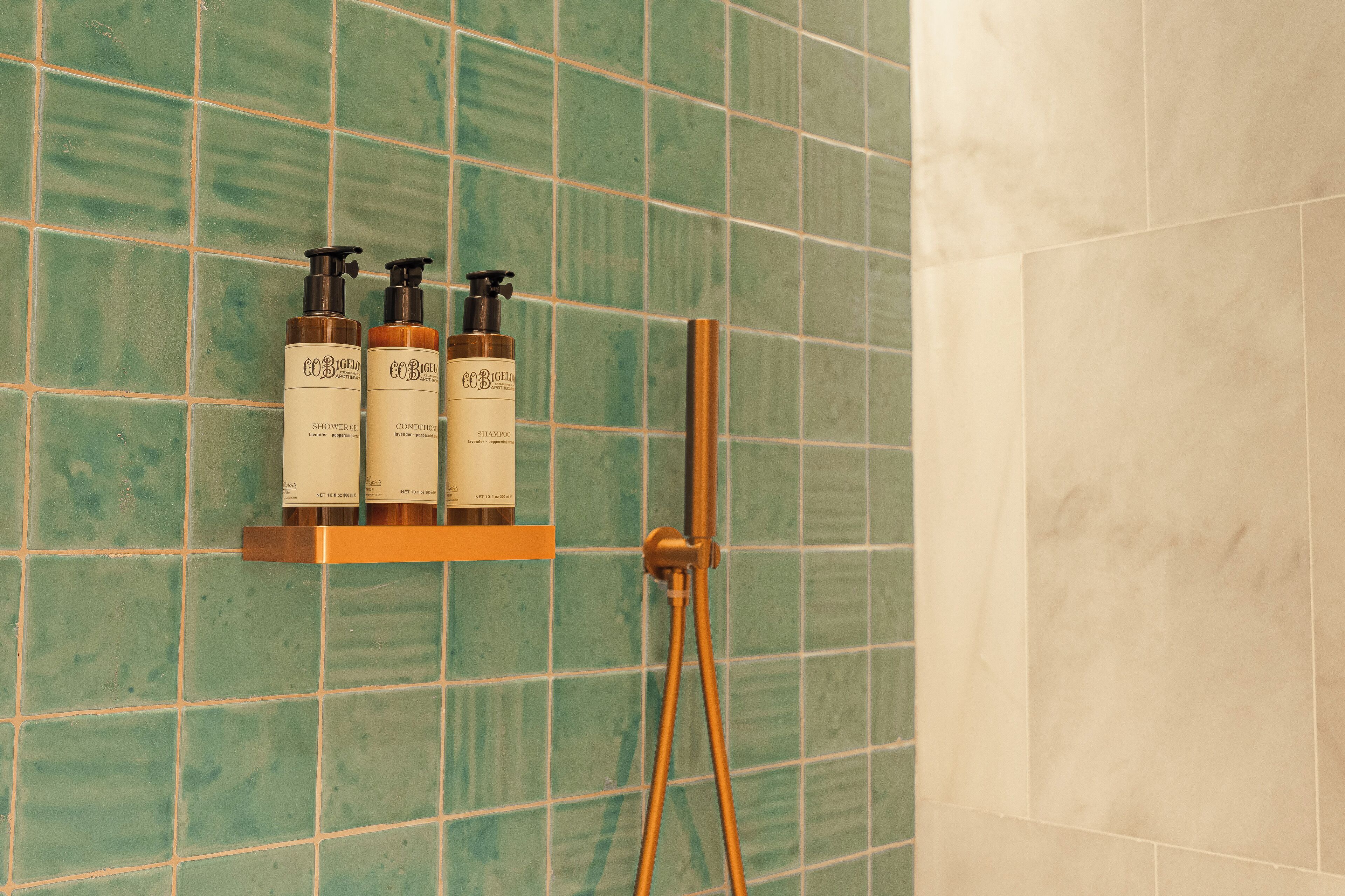 Un baño con azulejos verdes, una ducha y un estante con tres botellas de champú y acondicionador.