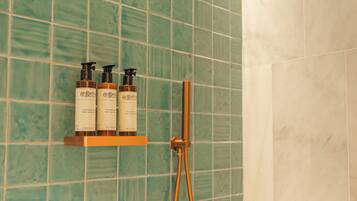 Un baño con azulejos verdes, una ducha y un estante con tres botellas de champú y acondicionador.