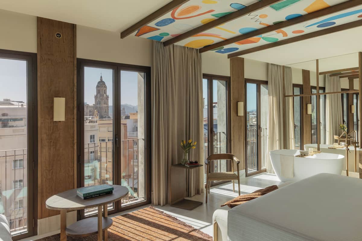Una habitación de hotel moderna con un ventanal grande, una mesa redonda, una silla, un sofá y una bañera.