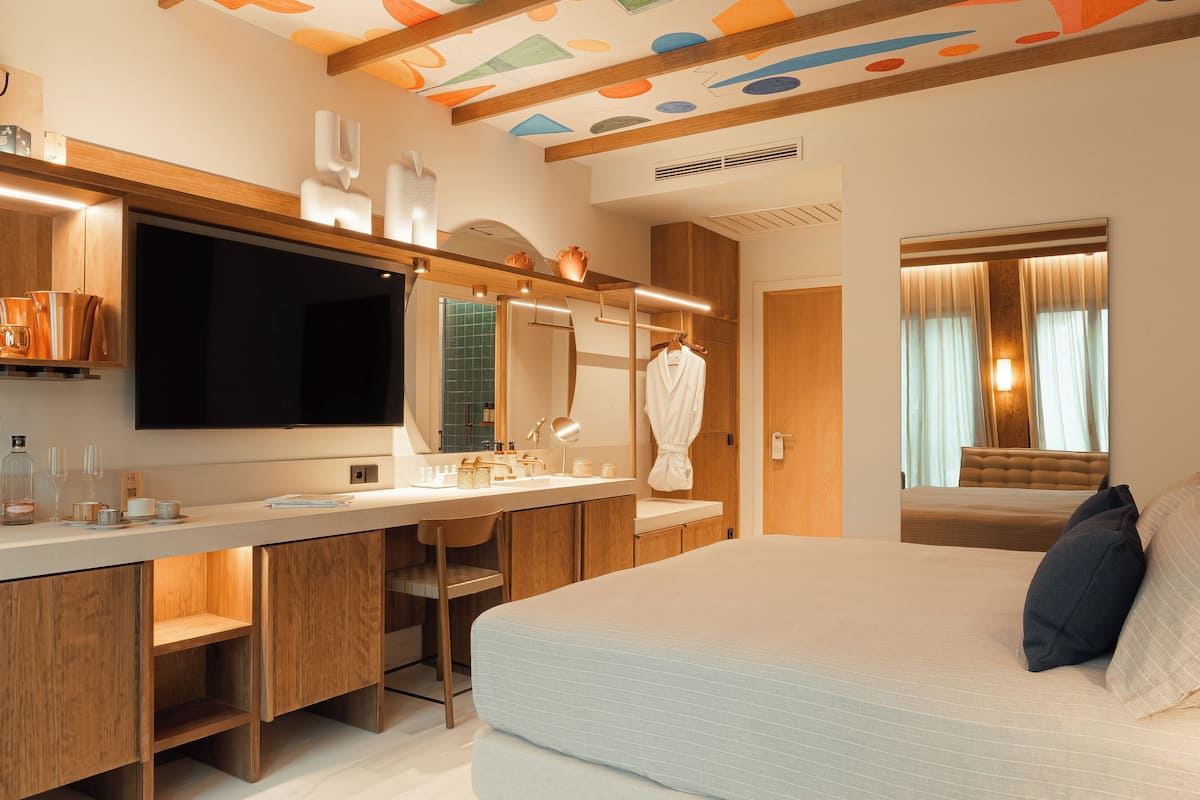 Una habitación de hotel moderna con una cama grande, un tocador con espejo, un televisor y un baño con ducha e inodoro.