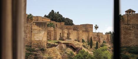 Una antigua fortaleza de piedra con una entrada destacada, rodeada de vegetación seca y árboles.
