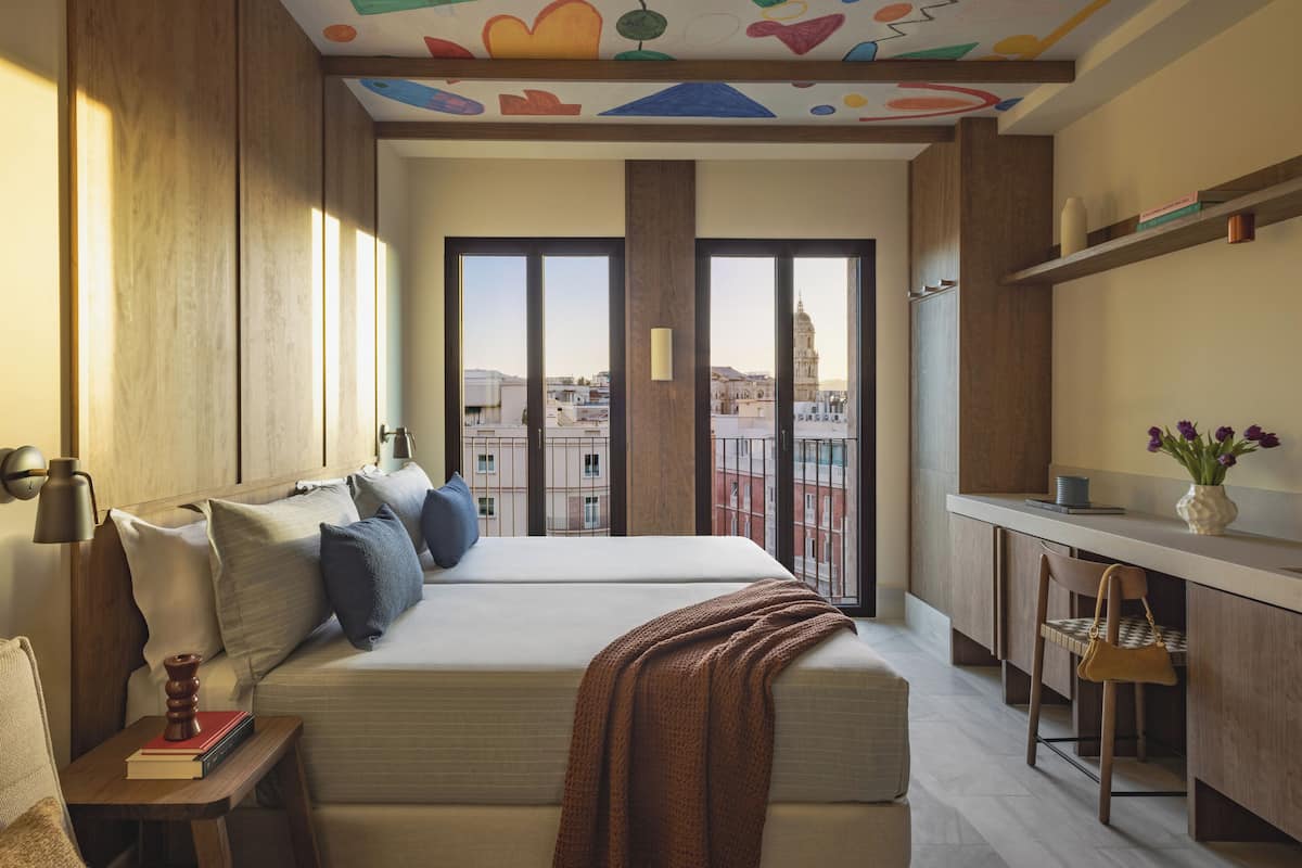 Un dormitorio moderno con una cama grande, mesitas de noche, un escritorio y vistas a la ciudad.