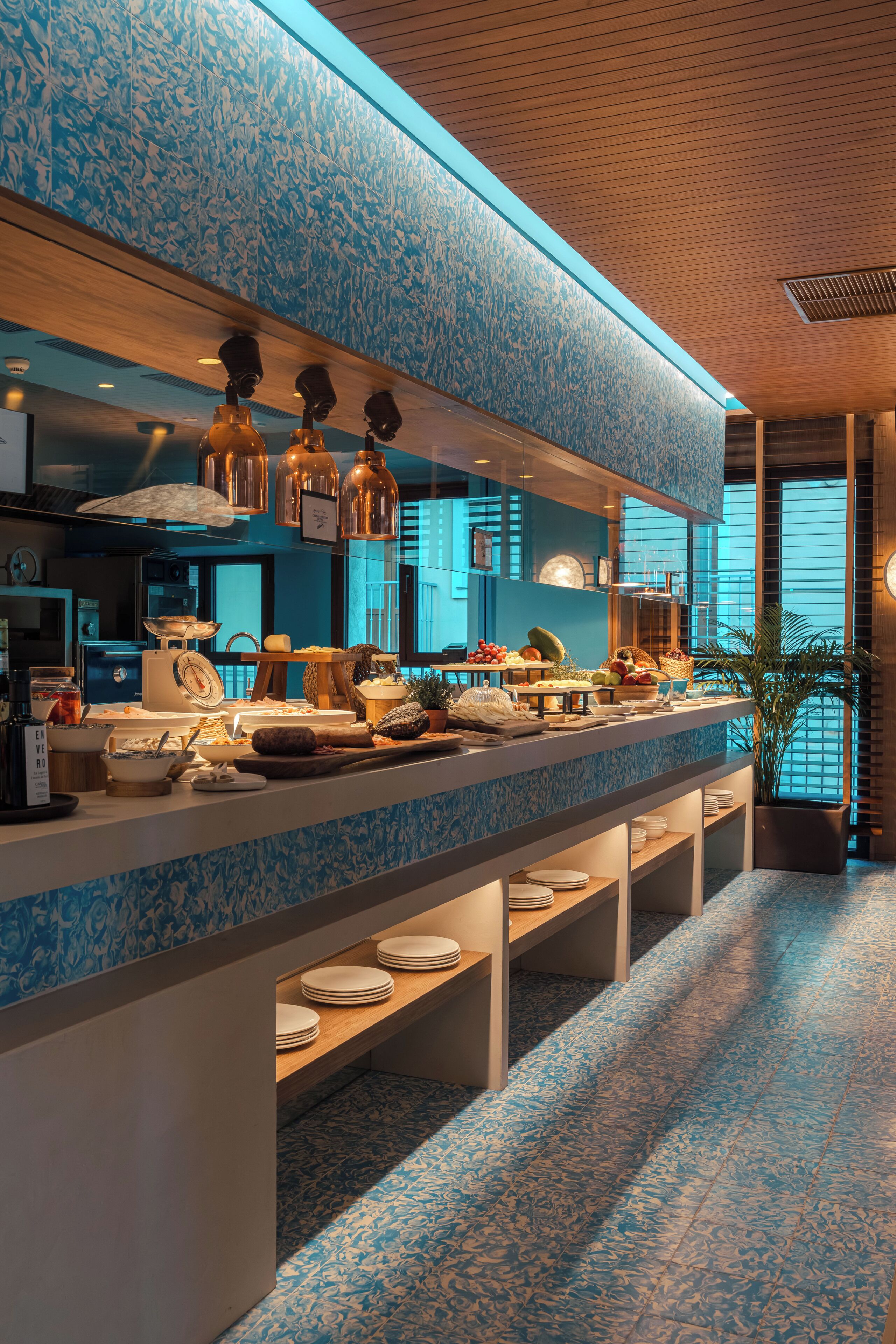 A modern hotel kitchen with a blue patterned backsplash, stainless steel appliances, and a buffet setup.