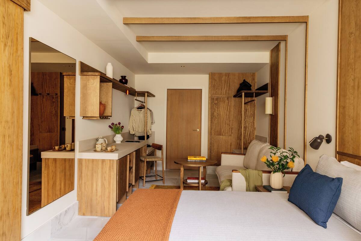 Ein modernes Hotelzimmer mit einem Bett, einem Schreibtisch mit Stuhl, einem Kleiderschrank und einer kleinen Sitzecke mit Sofa und Tisch.