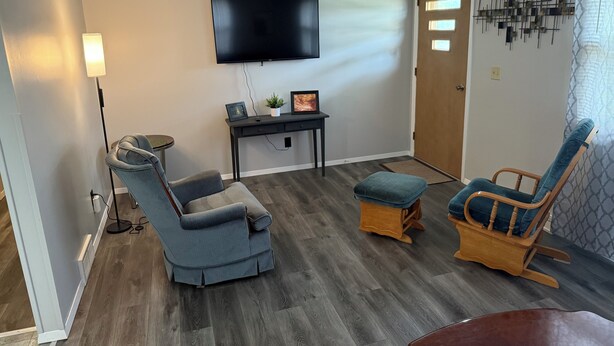 A living room with a grey sofa, a wooden rocking chair, a small table with a TV, and a floor lamp. - Darlington River View House - Direct Trail Access (Darlington)